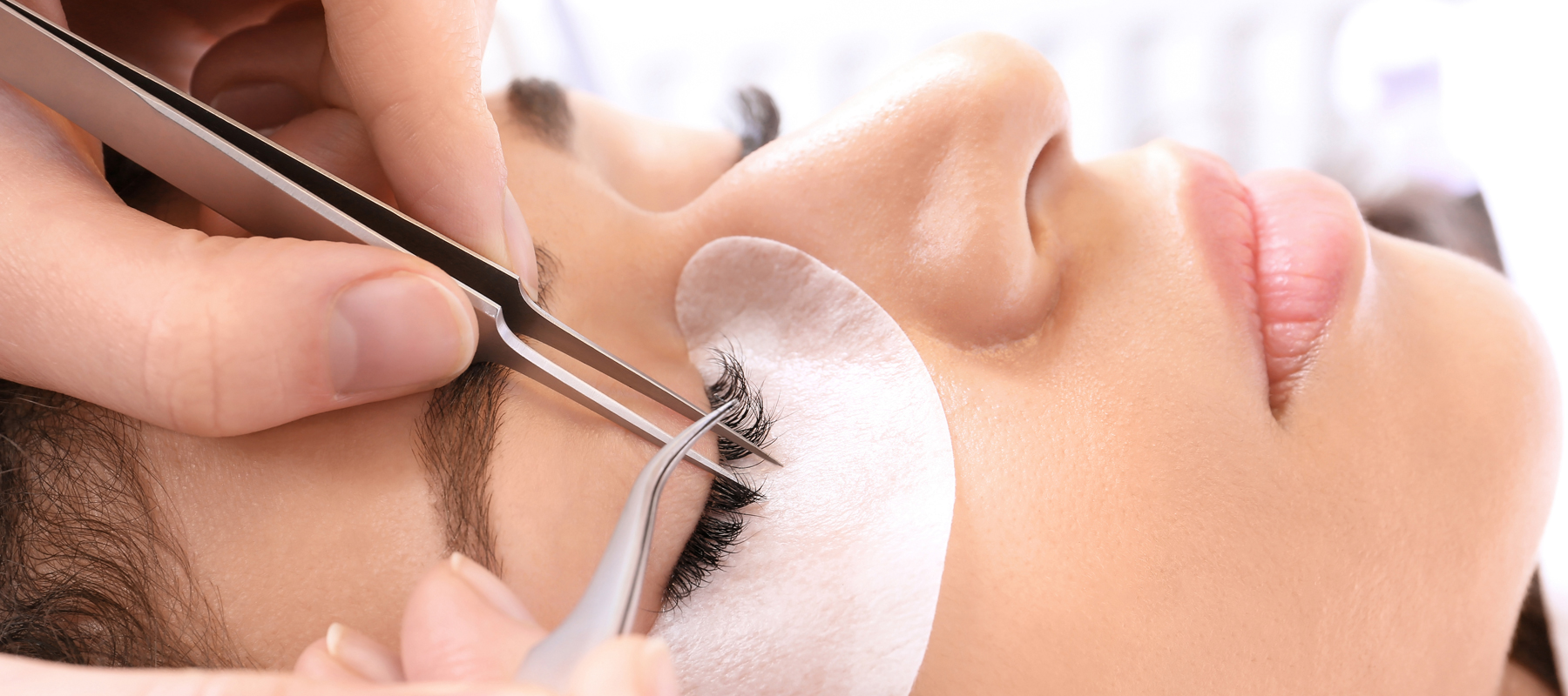 Young woman undergoing eyelash extensions procedure, closeup